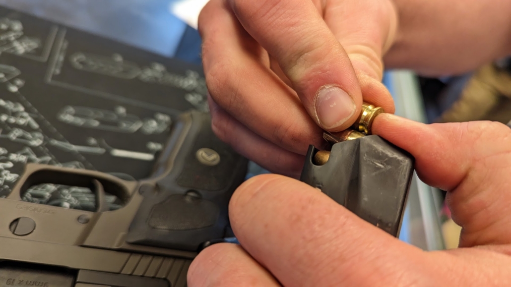 A close-up of hands loading bullets into a black gun magazine